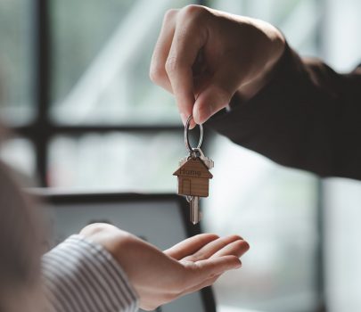 A home rental company employee is handing the house keys to a customer who has agreed to sign a rental contract, explaining the details and terms of the rental. Home and real estate rental ideas.